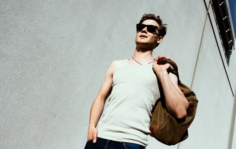 Mann med hvit singlett og skulderbag går ned trapp 