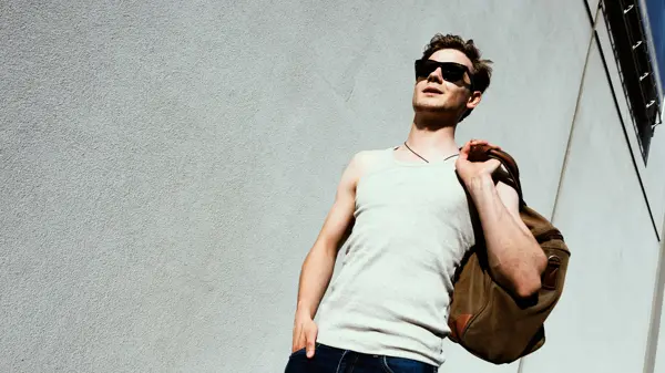 Mann med hvit singlett og skulderbag går ned trapp 