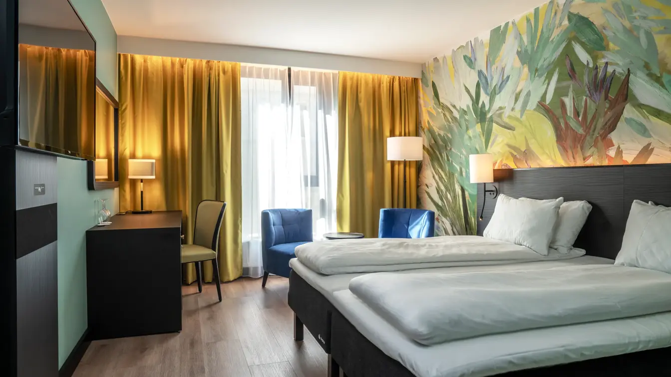 To enkeltsenger, TV, skrivebord, to blå lenestoler, gule gardiner, vindu