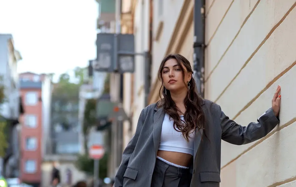 Dame med grå blazer og grå shorts poserer på gata foran vegg  