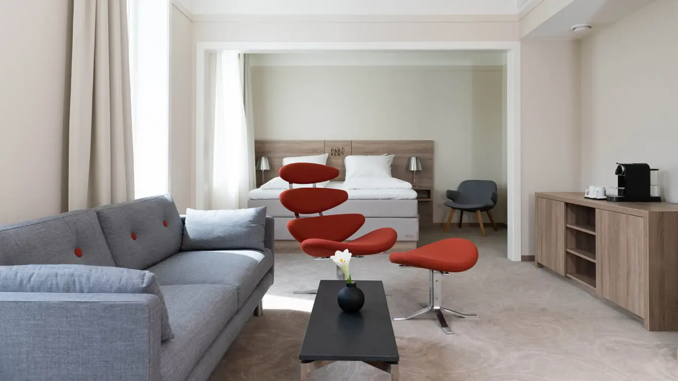 Bilde av sofa, bord og stol med dobbeltseng i bakgrunnen