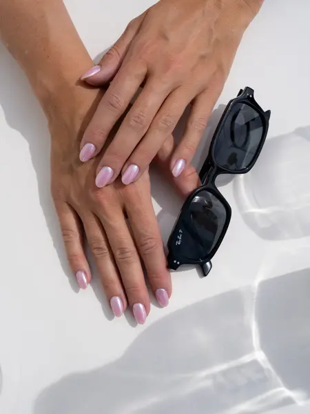 Hender på et bord med lakkerte negler og et par smale firkantede solbriller ved siden av.