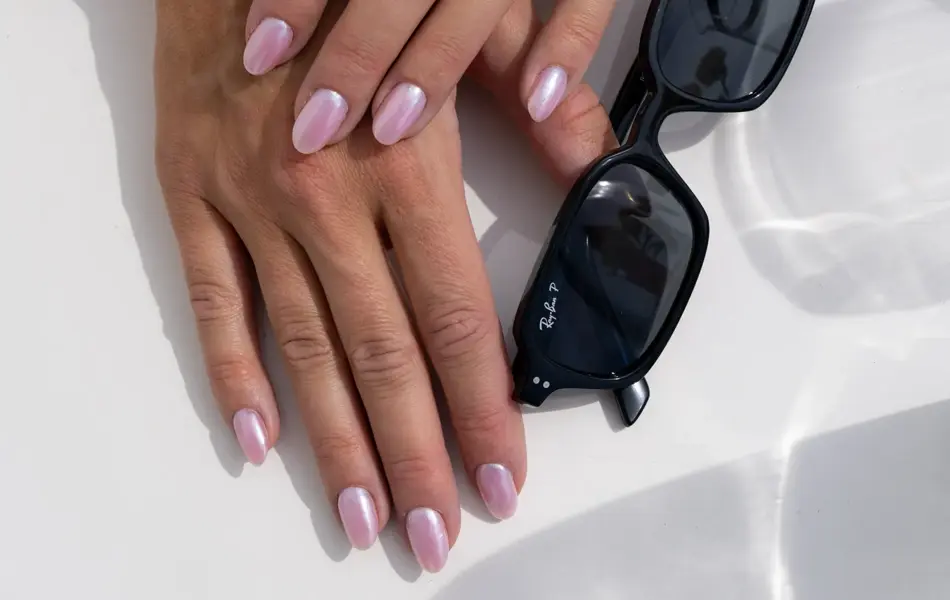 Hender på et bord med lakkerte negler og et par smale firkantede solbriller ved siden av.