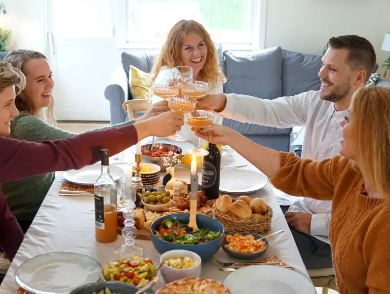 Dekket bord med mat og folk som smiler og skåler