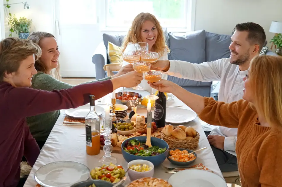 Dekket bord med mat og folk som smiler og skåler