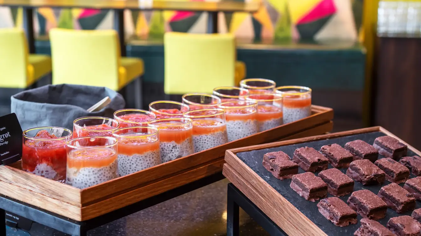 Brownies i terninger, chiapuding i små glass, gul vegg og gule stoler i bakgrunnen. 