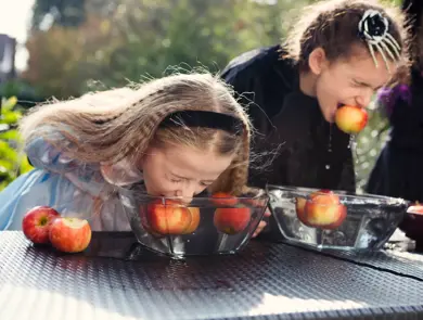 To jenter som spiser epler i en bolle med vann uten å bruke hendene