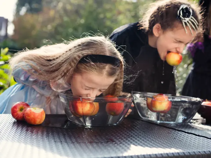 To jenter som spiser epler i en bolle med vann uten å bruke hendene