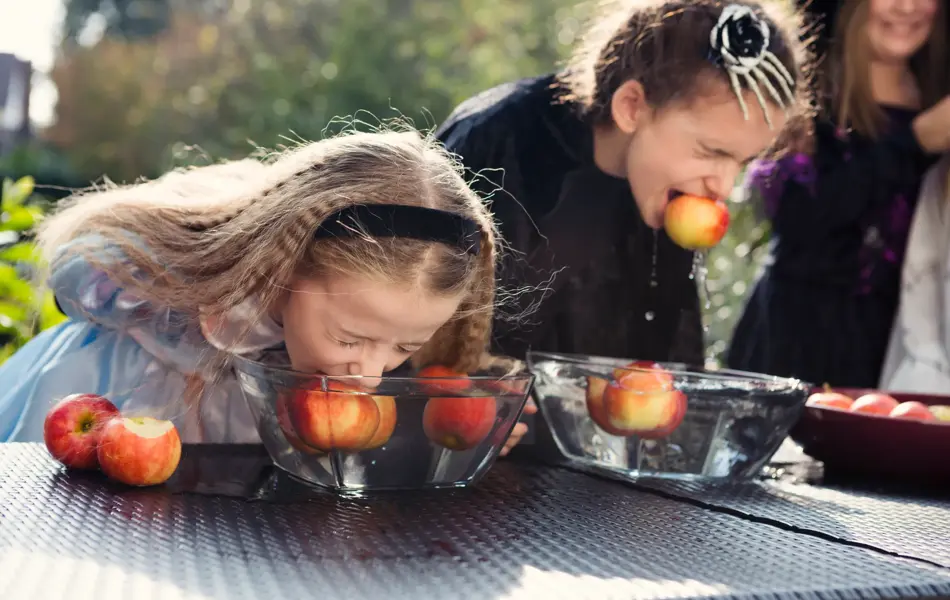 To jenter som spiser epler i en bolle med vann uten å bruke hendene
