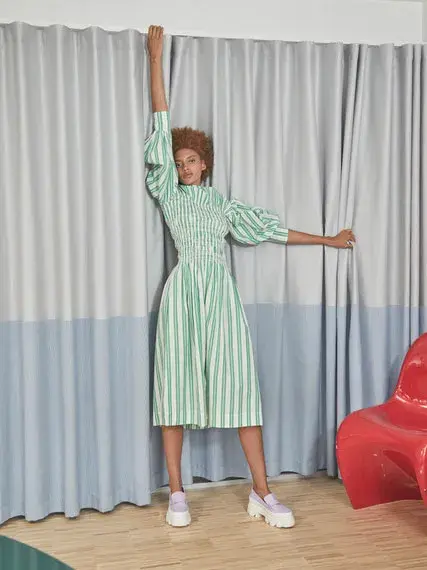 kvinnelig modell foran gardine, iført hvit og grønn stripete kjole