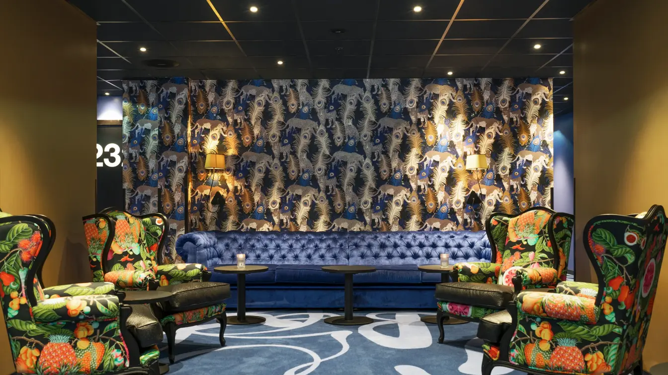 Teppe med mønster og påfugl-tapet, mønstrede lenestoler og blå sofa i lounge på Thon Hotel Terminus i Oslo sentrum nær Jernbanetorget