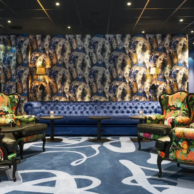 Teppe med mønster og påfugl-tapet, mønstrede lenestoler og blå sofa i lounge på Thon Hotel Terminus i Oslo sentrum nær Jernbanetorget