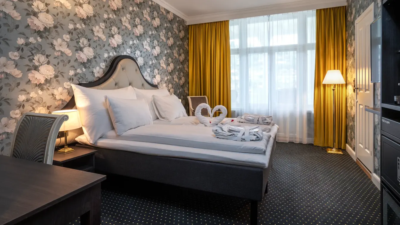 Dobbeltseng, svanehåndkle, rødes roseblader, morgenkåpevindu, gule gardiner, tapetvegg, stol, skrivebord, gulvlampe