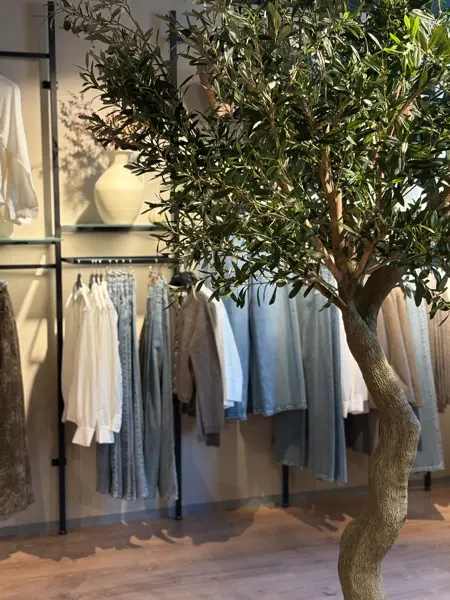 Klær som henger på vegg i fargene olablått og hvitt, og foran står et stort tre med grønne blader
