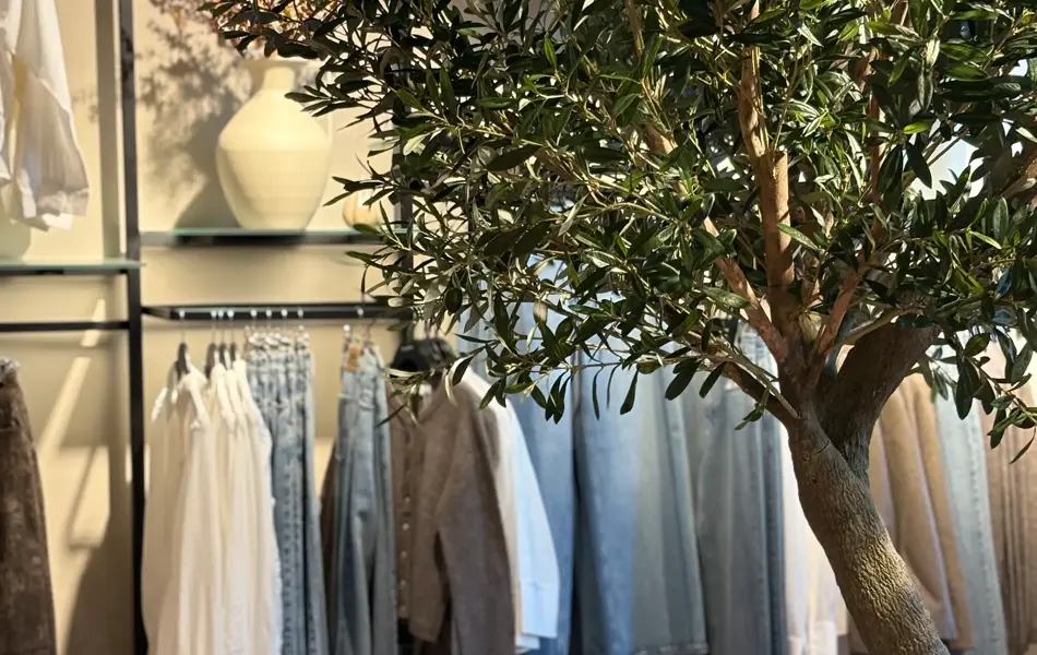 Klær som henger på vegg i fargene olablått og hvitt, og foran står et stort tre med grønne blader