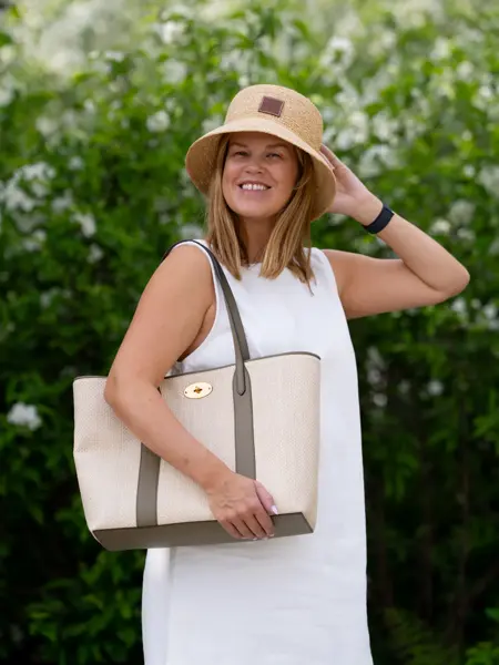 Damemodell står ute med hvit kjole lys beige strandveske og stråhatt