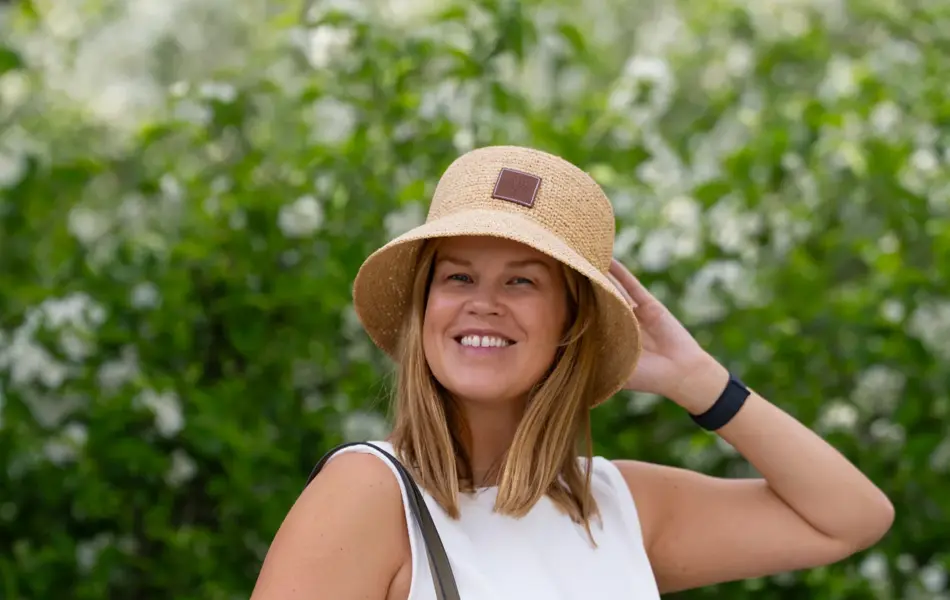 Damemodell står ute med hvit kjole lys beige strandveske og stråhatt