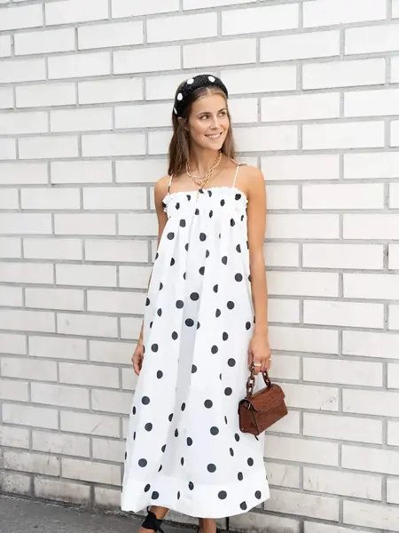 Ung kvinne kledd i hvit og prikkete kjole foran en hvit murvegg