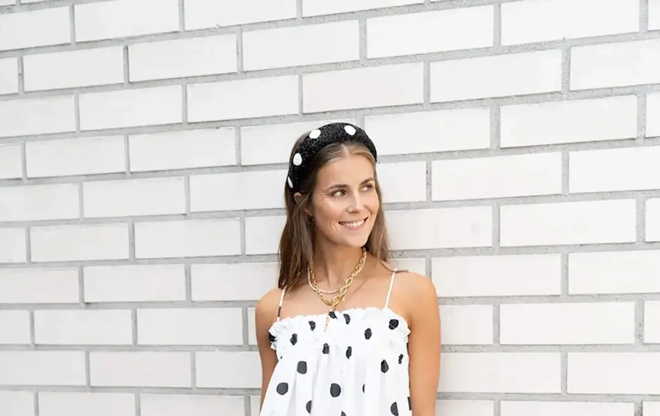 Ung kvinne kledd i hvit og prikkete kjole foran en hvit murvegg