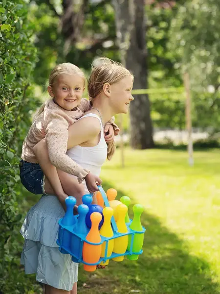 Stor jente bærer liten jente med bowlingkjegler i håden