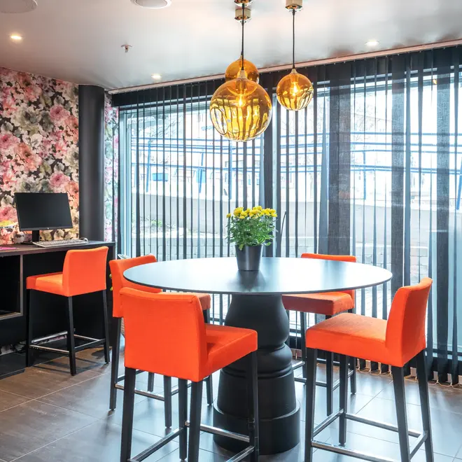 Oransje barstoler, rundt sort bord, fargerik blomstertaper og gjest PC i resepsjonen på Thon Hotel Hammerfest