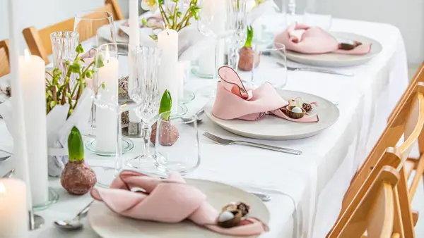 Langbord dekker til gjester med rosa servietter og grønn naturlig dekorasjon