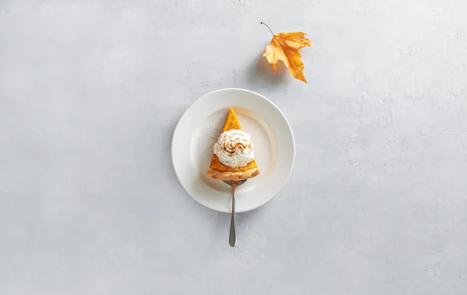 Pumpkin pie piece of cut, served on a plate, top down view, fall culinary concept