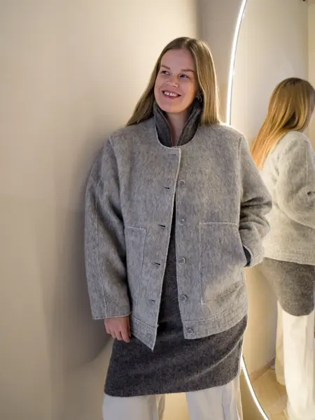 Dame i brunmelert jakke, grå ullkjole og hvite bukser