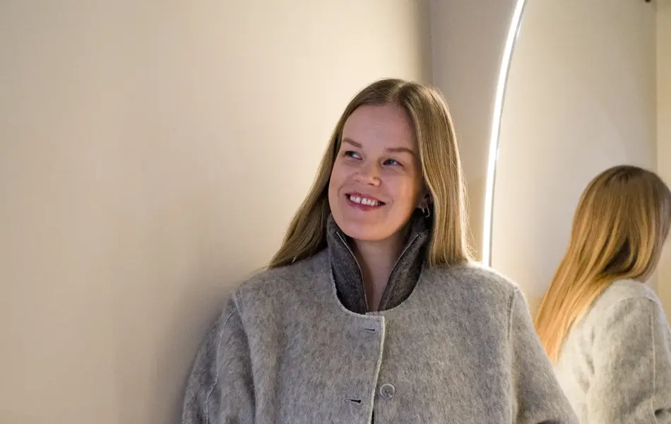 Dame i brunmelert jakke, grå ullkjole og hvite bukser