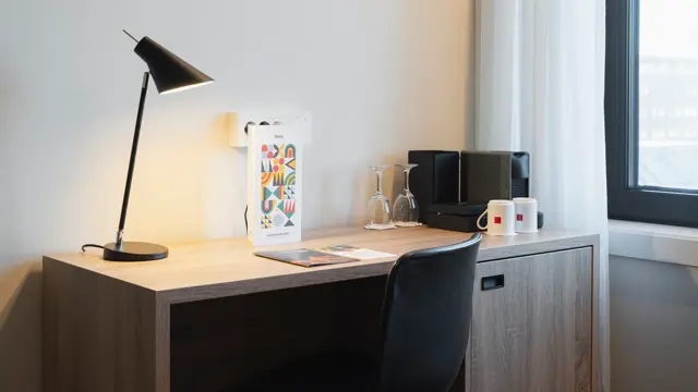 Skrivebord på business rom, med bordlampe, espresso maskin, kaffekopper og lite kjøleskap under.