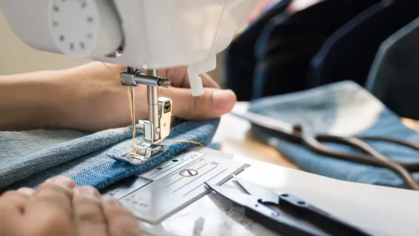 Closep up tailor process, women's hand working on sewing machine sew denim fabric