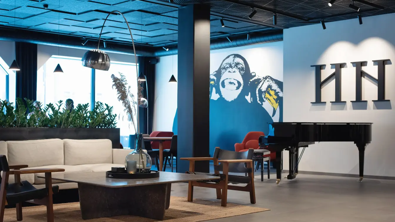 Hvit sofa og mørke stoler rundt et lavt sort bord. Hvit vegg med en stort malt ape på.  I lobbyen på Thon Hotel Norge i Kristiansand.