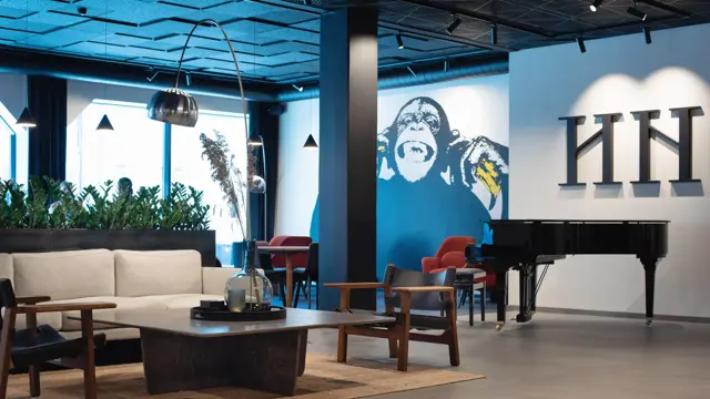Hvit sofa og mørke stoler rundt et lavt sort bord. Hvit vegg med en stort malt ape på.  I lobbyen på Thon Hotel Norge i Kristiansand.