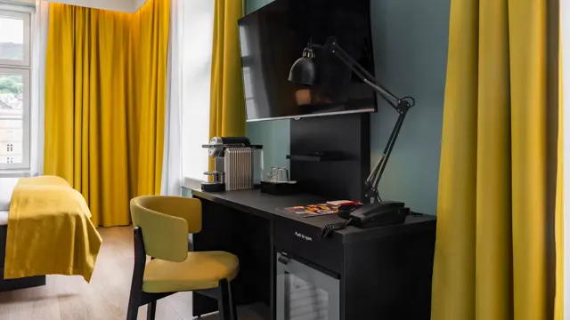Superior rom med skrivebord, kjøleskap, vegghengt TV, turkise vegger og gule gardiner.