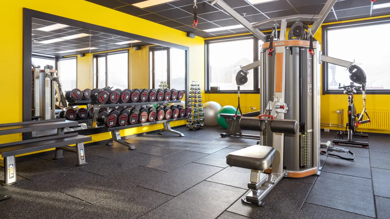 Treningsrom med forskjellige treningsapparater, gul vegg og utsikt fra vinduet på Thon Hotel Kirkenes ved kaia i Kirkenes sentrum