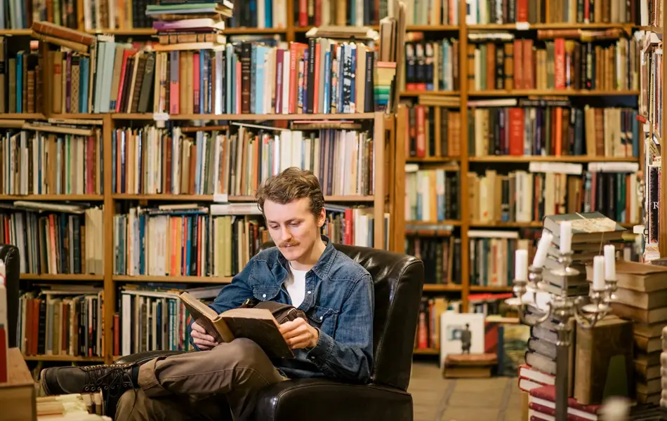 Mann sitter i lenestol og leser, bokhylle i uskarp bakgrunn. Foto til artikkel om julegave far blir glad for