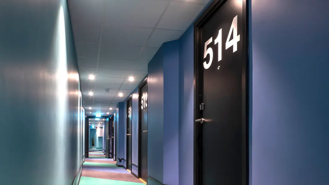 Korridor med fargerik bred stripete teppe, blå vegger og store hvit romnummer på sorte dører på Thon Hotel Astoria i Oslo 