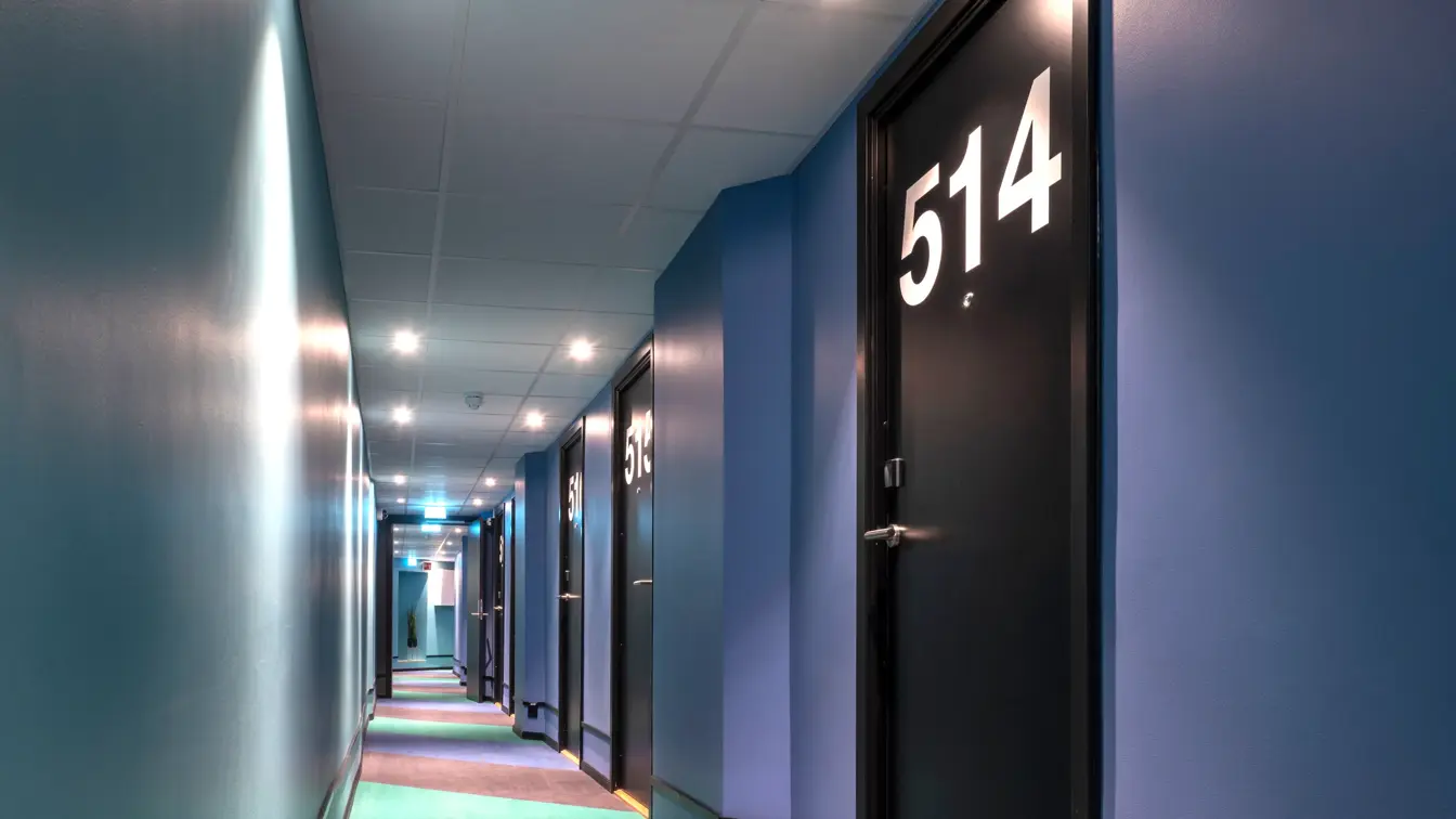 Korridor med fargerik bred stripete teppe, blå vegger og store hvit romnummer på sorte dører på Thon Hotel Astoria i Oslo 