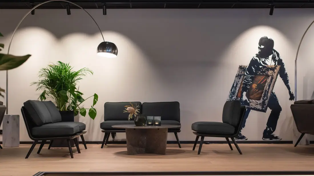 I lobbyen på Thon Hotel Norge i Kristiansand, med mørke sofaer rundt et lavt mørkt bord, grønne vekster. Hvit vegg med street art, hvor en person med finlandshette holder et innrammet Skrik-maleri under armen.