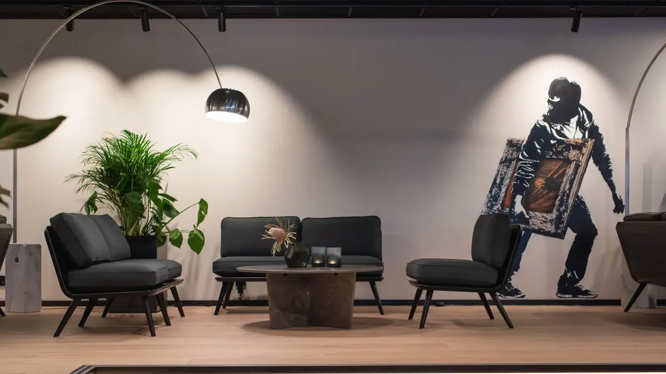 I lobbyen på Thon Hotel Norge i Kristiansand, med mørke sofaer rundt et lavt mørkt bord, grønne vekster. Hvit vegg med street art, hvor en person med finlandshette holder et innrammet Skrik-maleri under armen.