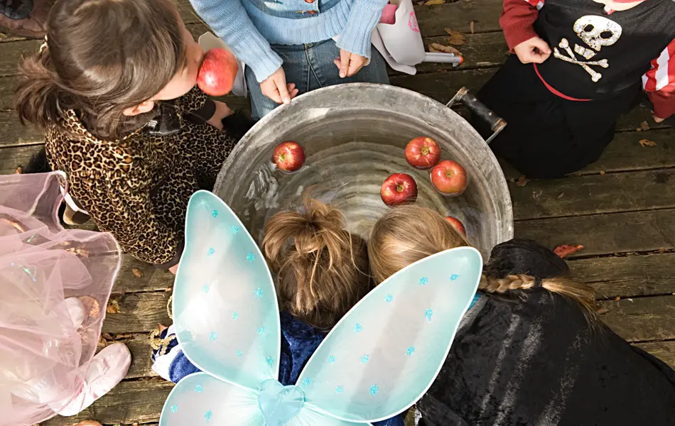 Barn biter i eple som ligger i stålbøtte med vann utkledd til halloween