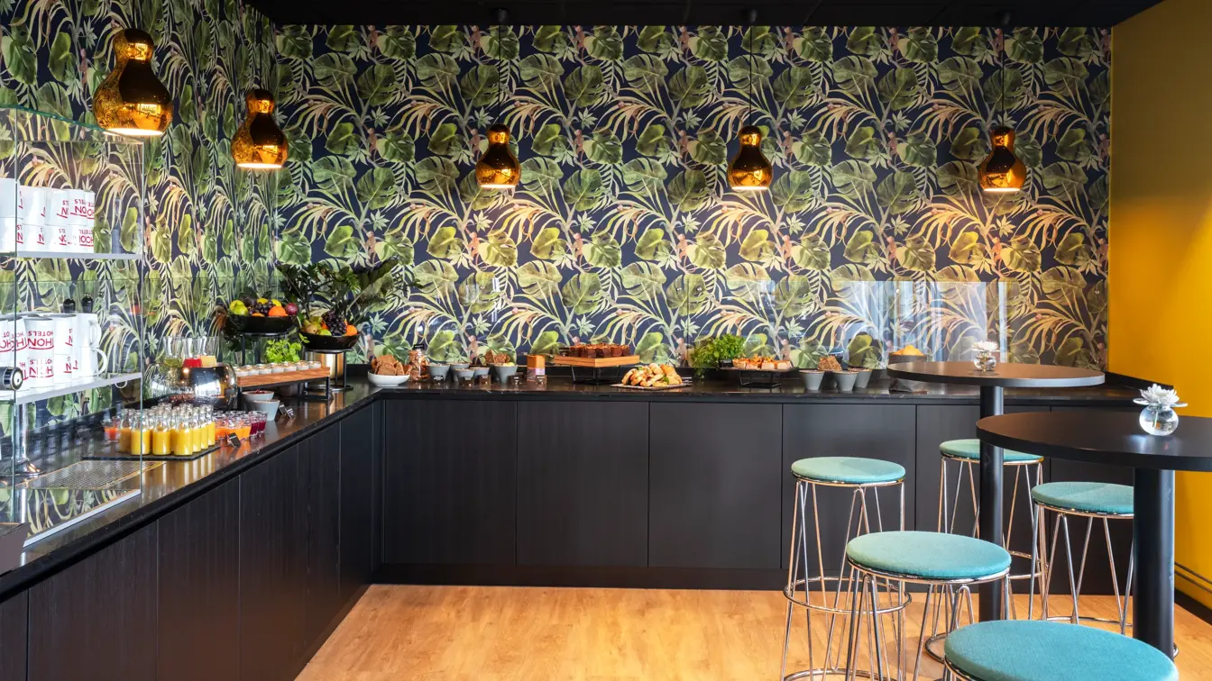 Tapetvegg med mønster, to runde bord med barkrakker, svart bordbenk med diverse pausesnack. 