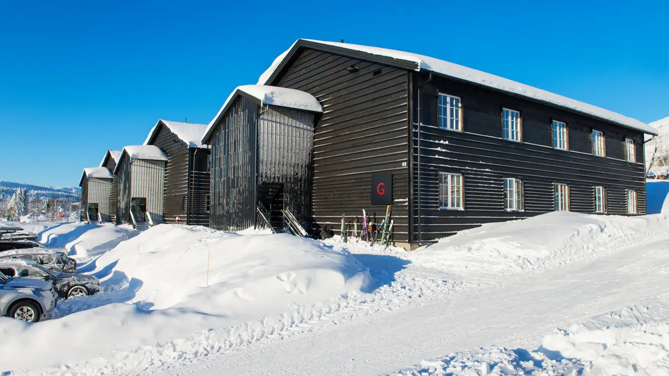 Bilde som viser boligprosjektet Skitorget. Leilighetsbygg som ligger rett ved skibakken. På bildet er det blå himmel og mye flott snø.