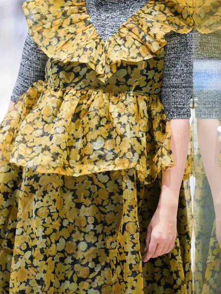 Jente som står og lener seg til en vegg med gul kjole og grå genser under