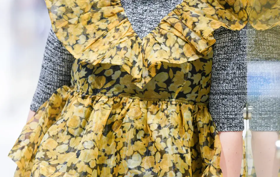 Jente som står og lener seg til en vegg med gul kjole og grå genser under