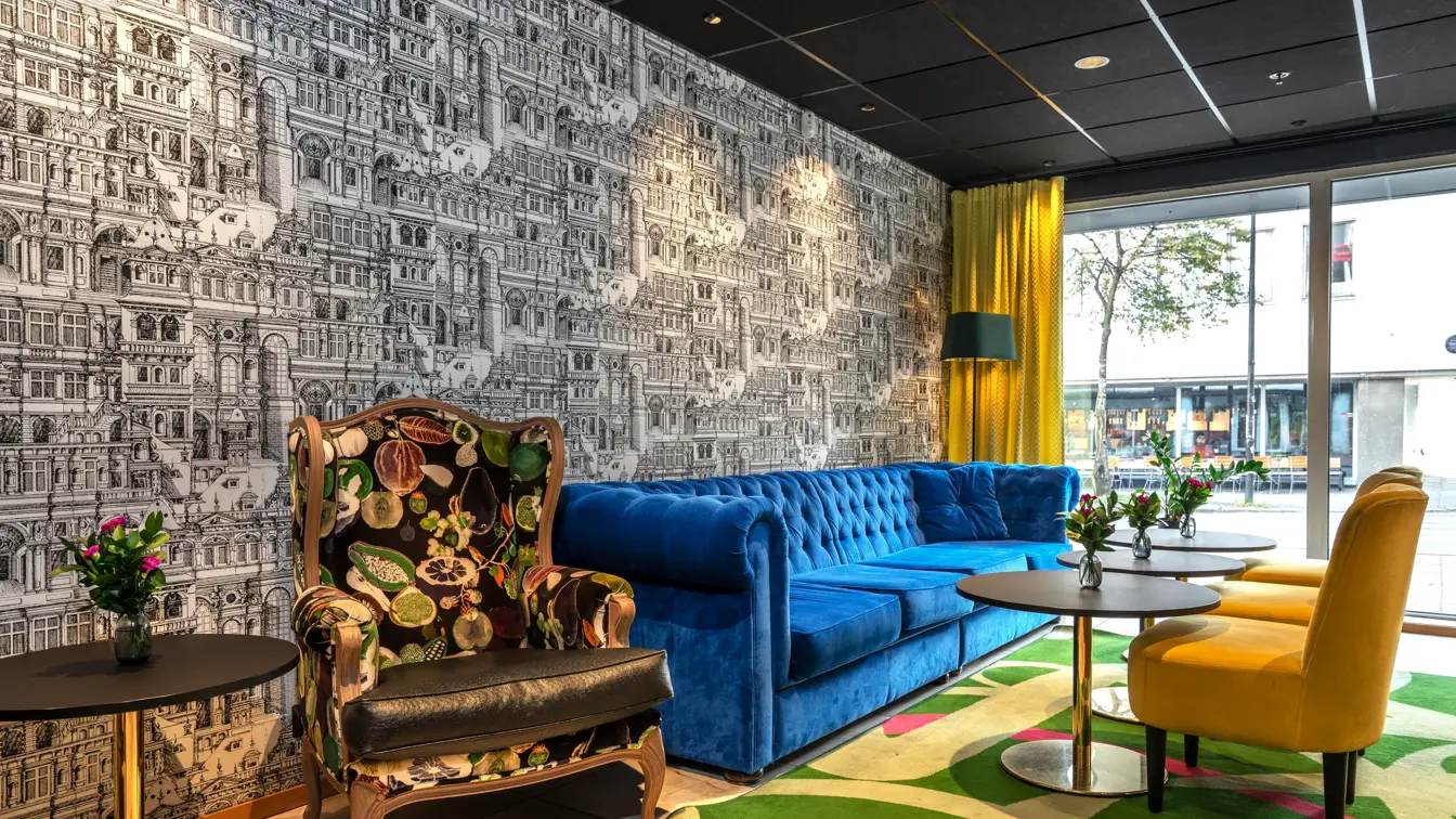 Lobbyområde med blå velour sofa, to gule lenestoler, mønstrete tapet og grønt gulvteppe