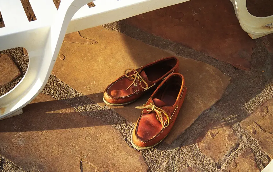 Nærbilde av brune seilersko med lærlisser stående på steingrunn under hvit solstol i plast 