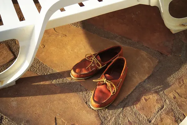 Nærbilde av brune seilersko med lærlisser stående på steingrunn under hvit solstol i plast 