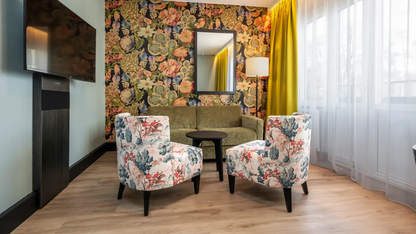 Business rom med sittegruppe, vegghengt TV, fargerik tapet og speil på veggen.