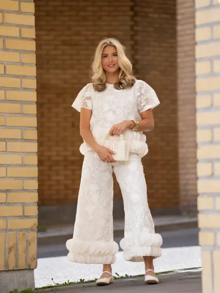 Ung jente med hvit topp og bukse, liten veske og ballerinasko